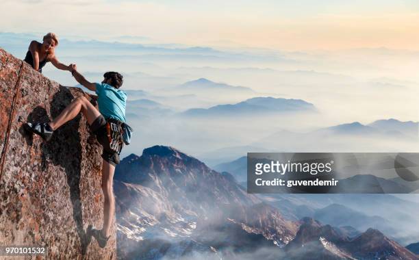 teamwork couple helping hand trust in inspiring mountains - clambering imagens e fotografias de stock