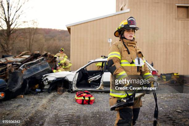 female firefighter holding machinery while standing on field against house - fireman stock pictures, royalty-free photos & images
