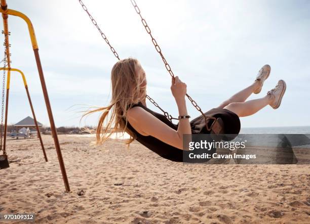 side view of woman playing on swing against sky - woman on swing stock-fotos und bilder