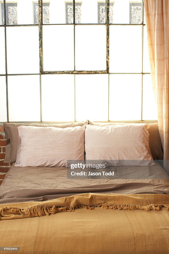 Empty bed in front of loft style windows