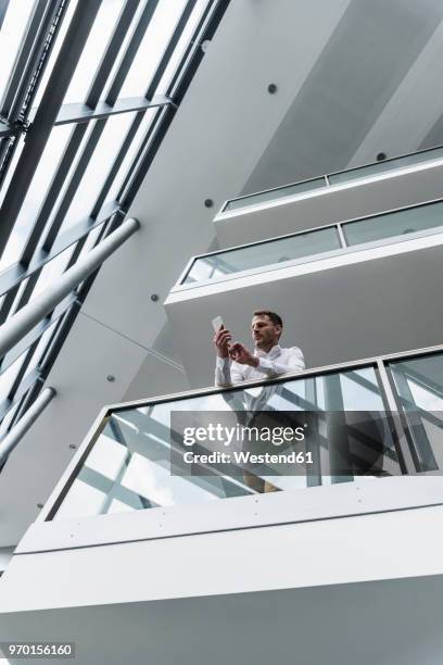 businessman in office building leaning on railing looking at cell phone - mobile phone reading low angle stock-fotos und bilder