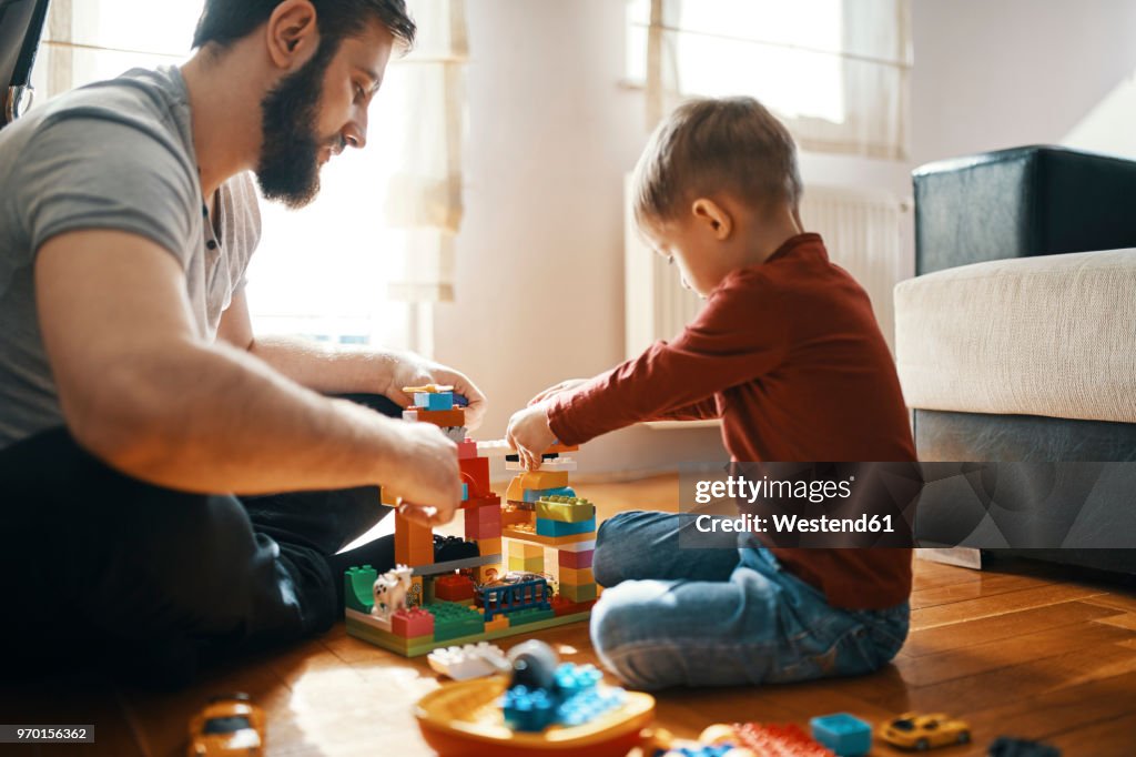 Father and son sitting on the floor playing together with building bricks