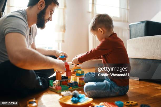 father and son sitting on the floor playing together with building bricks - bloque de madera fotografías e imágenes de stock