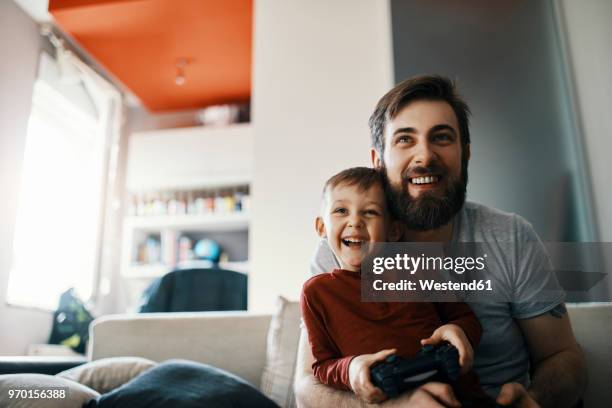 father and son sitting together on the couch playing computer game - dad son foto e immagini stock