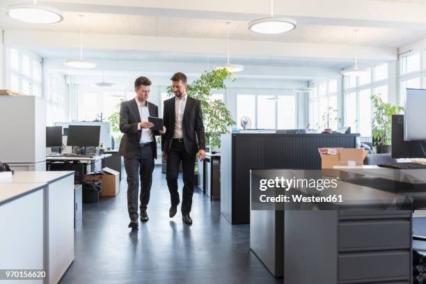 two businessmen walking in office, using digital tablet, talking - business men walking stock pictures, royalty-free photos & images