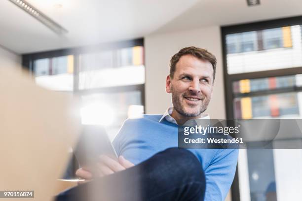 smiling businessman using tablet in office - looking away stock-fotos und bilder