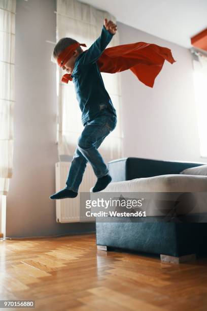 little boy dressed up as a superhero playing at home - jump on sofa stock-fotos und bilder
