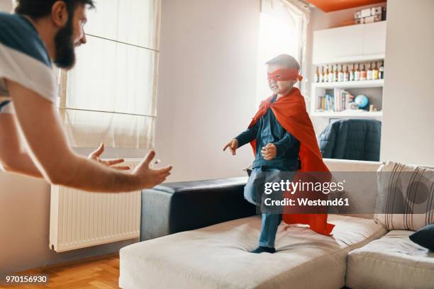 father playing with his little son dressed up as a superhero at home - raufen stock-fotos und bilder