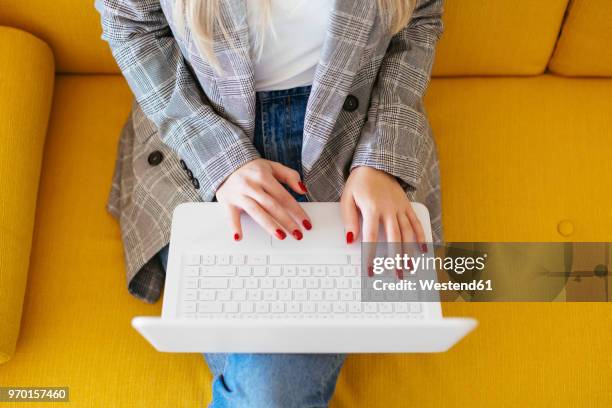 businesswoman sitting on yellow couch, using laptop - red nail polish stock-fotos und bilder