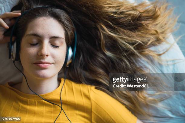 portrait of smiling young woman lying on bed listening music with headphones - listening stock pictures, royalty-free photos & images