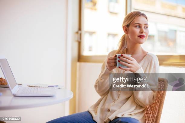 blonde woman with cup of coffee looking out of the window - coffee window stock pictures, royalty-free photos & images