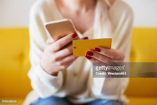 blonde woman using smartphone and using bank card at home - internetbankieren stockfoto's en -beelden