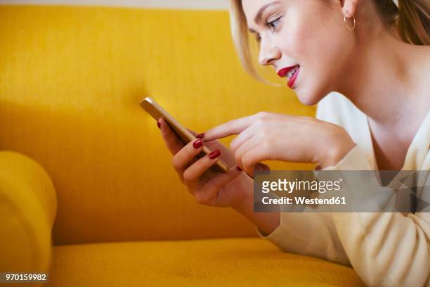 blonde woman lying on sofa, using smartphone at home - solo una donna giovane foto e immagini stock