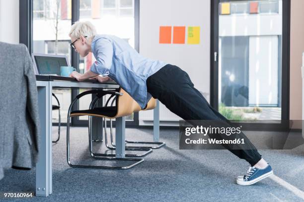 businesswoman in office doing push ups on desk - business woman movement dynamic stock-fotos und bilder