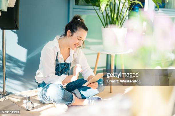 smiling young freelancer sitting on the floor in her studio using tablet - fashion woman floor cross legged stock pictures, royalty-free photos & images