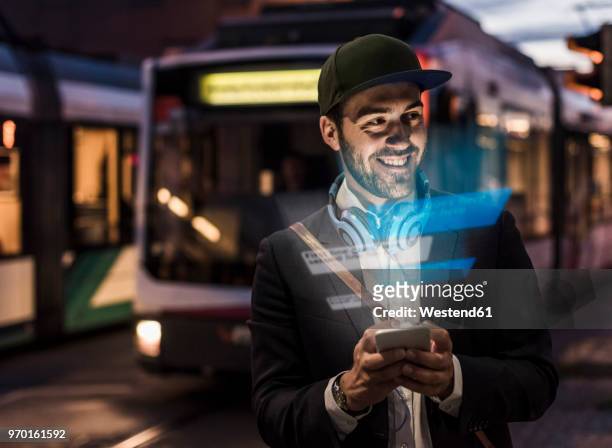 young man outdoors at dusk with text emerging from smartphone - bus sign photos et images de collection