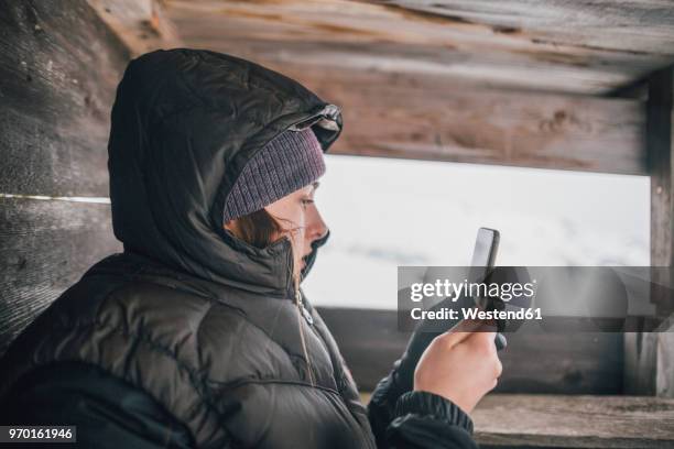 austria, kitzbuehel, young woman in raised hide looking at cell phone in winter - le cap - fotografias e filmes do acervo