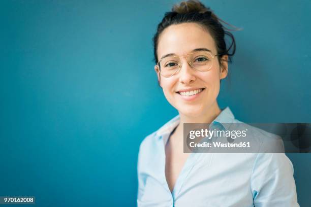 portrait of smiling young woman wearing glasses in front of blue wall - portrait blue background stock-fotos und bilder