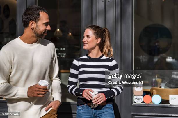 man and woman holding takeaway cups outside a cafe talking - flirten stock-fotos und bilder