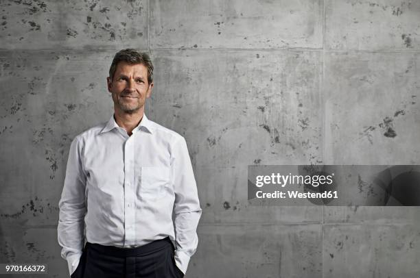 portrait of smiling mature man in front of concrete wall - camisa blanca fotografías e imágenes de stock