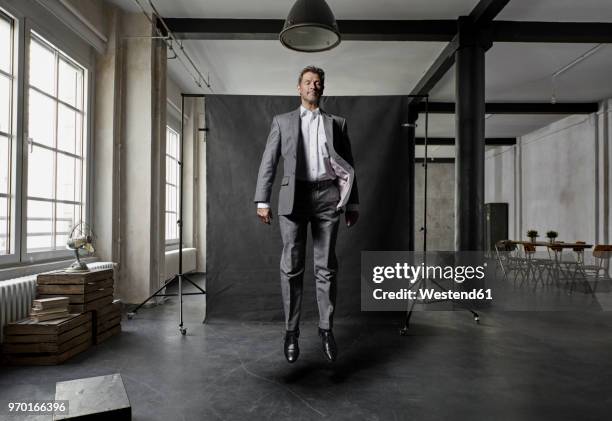 mature businessman floating in front of black backdrop in loft - helden stock-fotos und bilder