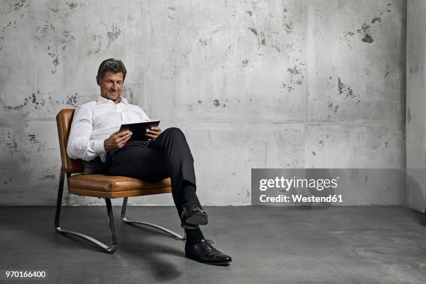 mature man using digital tablet in front of concrete wall - sitz stock-fotos und bilder