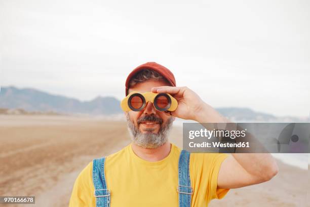 bearded man using binoculars on the beach - verrekijker stockfoto's en -beelden