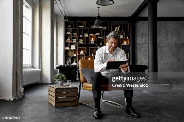 smiling mature man using digital tablet in loft - executive man sitting at home stock pictures, royalty-free photos & images