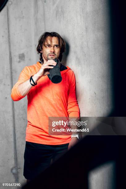 athlete wearing standing at concrete wall drinking from flask - drinking flask stock pictures, royalty-free photos & images