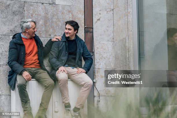 confident senior man and young man sitting in the city talking - origins imagens e fotografias de stock