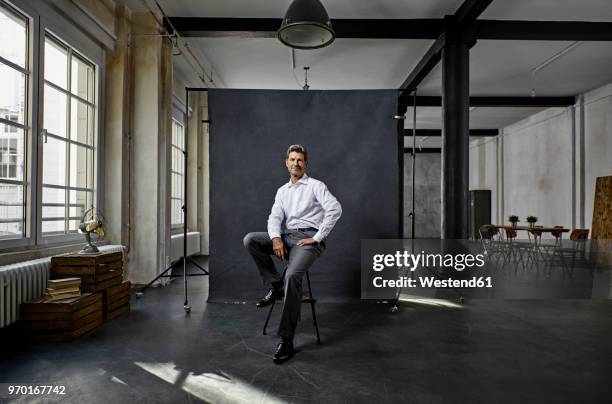 portrait of mature businessman in front of black backdrop in loft - white/black shirt stock-fotos und bilder