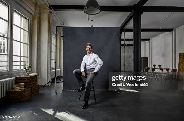 portrait of mature businessman in front of black backdrop in loft - businessman sitting stock pictures, royalty-free photos & images