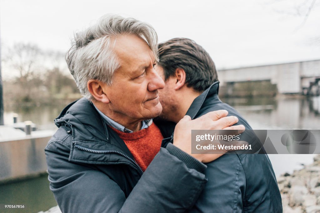 Young man and senior man embracing at the riverside