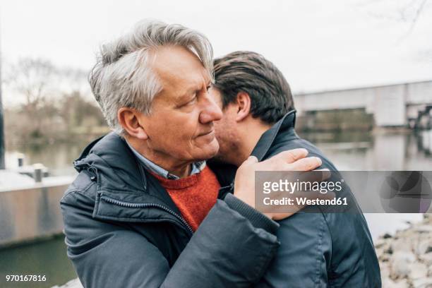 young man and senior man embracing at the riverside - mourning imagens e fotografias de stock