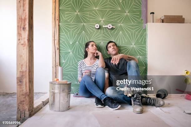couple renovating new house, sitting on ground planning bathroom - renovations stockfoto's en -beelden