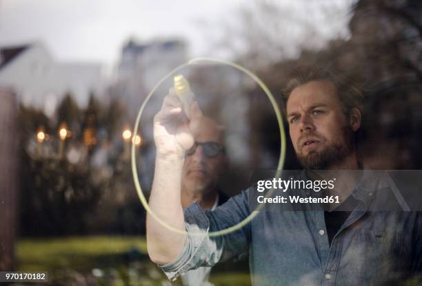 mature man drawing a circle on window pane, senior man watching - people doing things together stock pictures, royalty-free photos & images