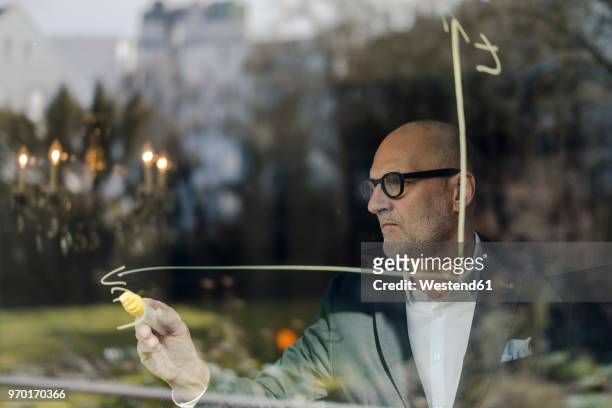 senior businessman brainstorming, drawing formulas on window pane - economy business and finance stock-fotos und bilder