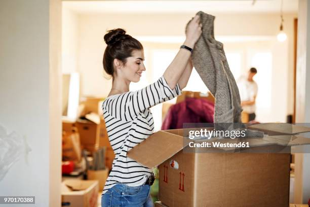 young woman moving house, unpacking cardboard boxes - packing boxes stockfoto's en -beelden