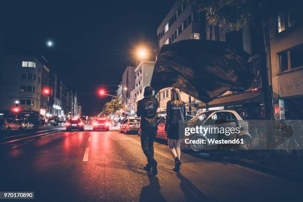 back view of young couple with black flag walking on the street by night - soziale gerechtigkeit stock-fotos und bilder