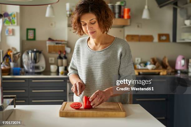 mature woman cutting tomato in kitchen - kitchen knife stockfoto's en -beelden