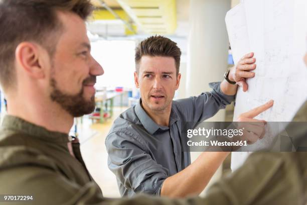 two men discussing plan in factory - rolling up sleeve stock-fotos und bilder