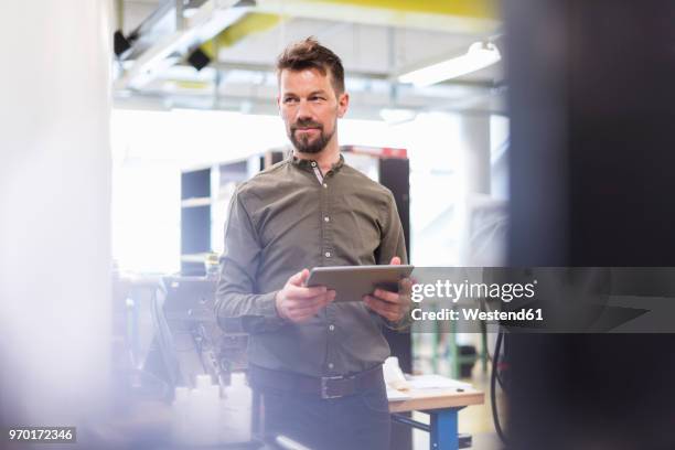 smiling man standing in factory with tablet looking sideways - mirar alrededor fotografías e imágenes de stock