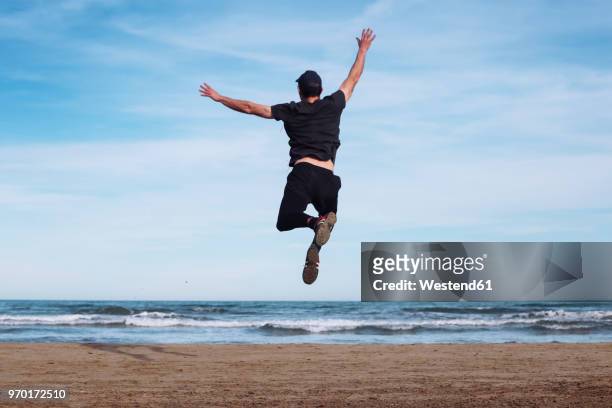 back view of man jumping in the air on the beach - man jumping stock pictures, royalty-free photos & images