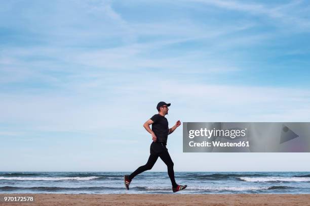 spain, man dressed in black jogging on the beach - ropa de deporte fotografías e imágenes de stock