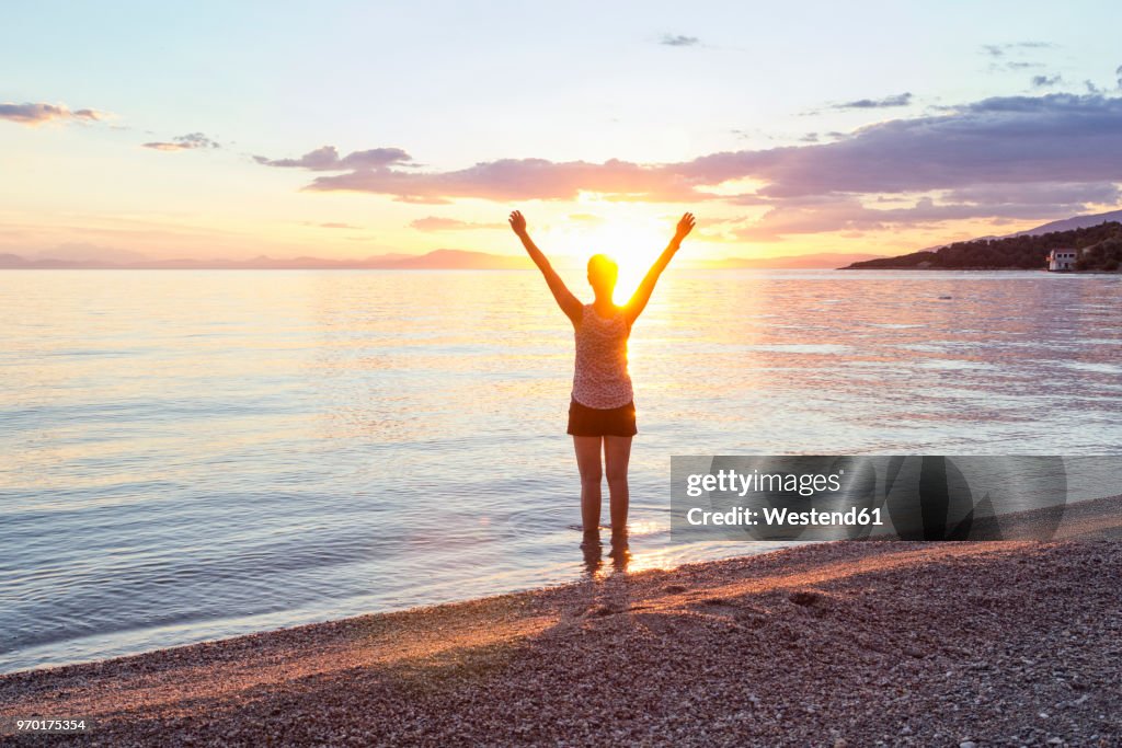 Greece, Pelion, Pagasetic Gulf, woman on the beach with raised arms at sunset, Kalamos in the background