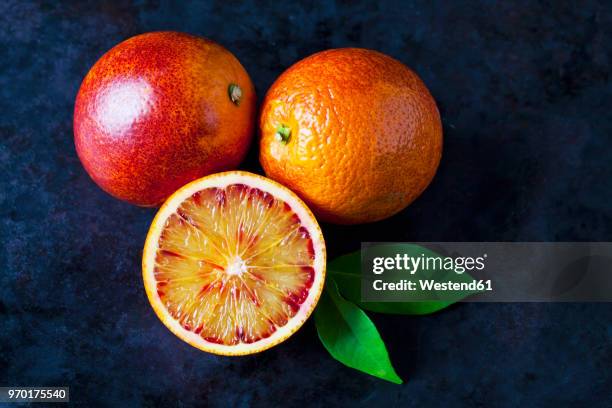 two whole and a half blood orange on dark ground - bloedsinaasappel stockfoto's en -beelden