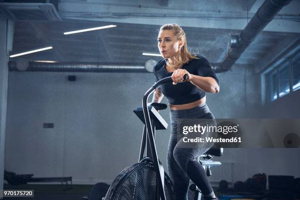 athletic woman doing airbike workout at gym - anstrengung stock-fotos und bilder