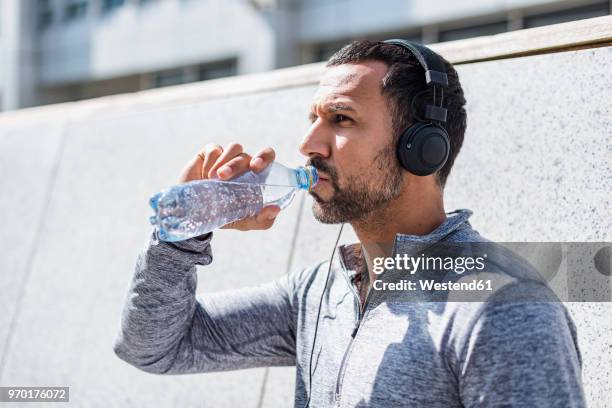 man having a break from exercising wearing headphones and drinking from bottle - man drinking water photos et images de collection