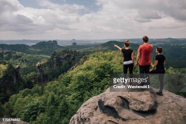 germany, saxony, elbe sandstone mountains, friends on a hiking trip standing on rock - vinden stockfoto's en -beelden