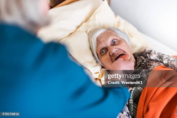 woman taking care of old woman lying in bed - gebiss mensch zähne stock-fotos und bilder